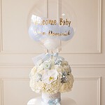 Arreglo de bienvenida al bebé: rosas marfil, hortensias y orquídea blanca en caja blanca con cinta celeste y globo burbuja