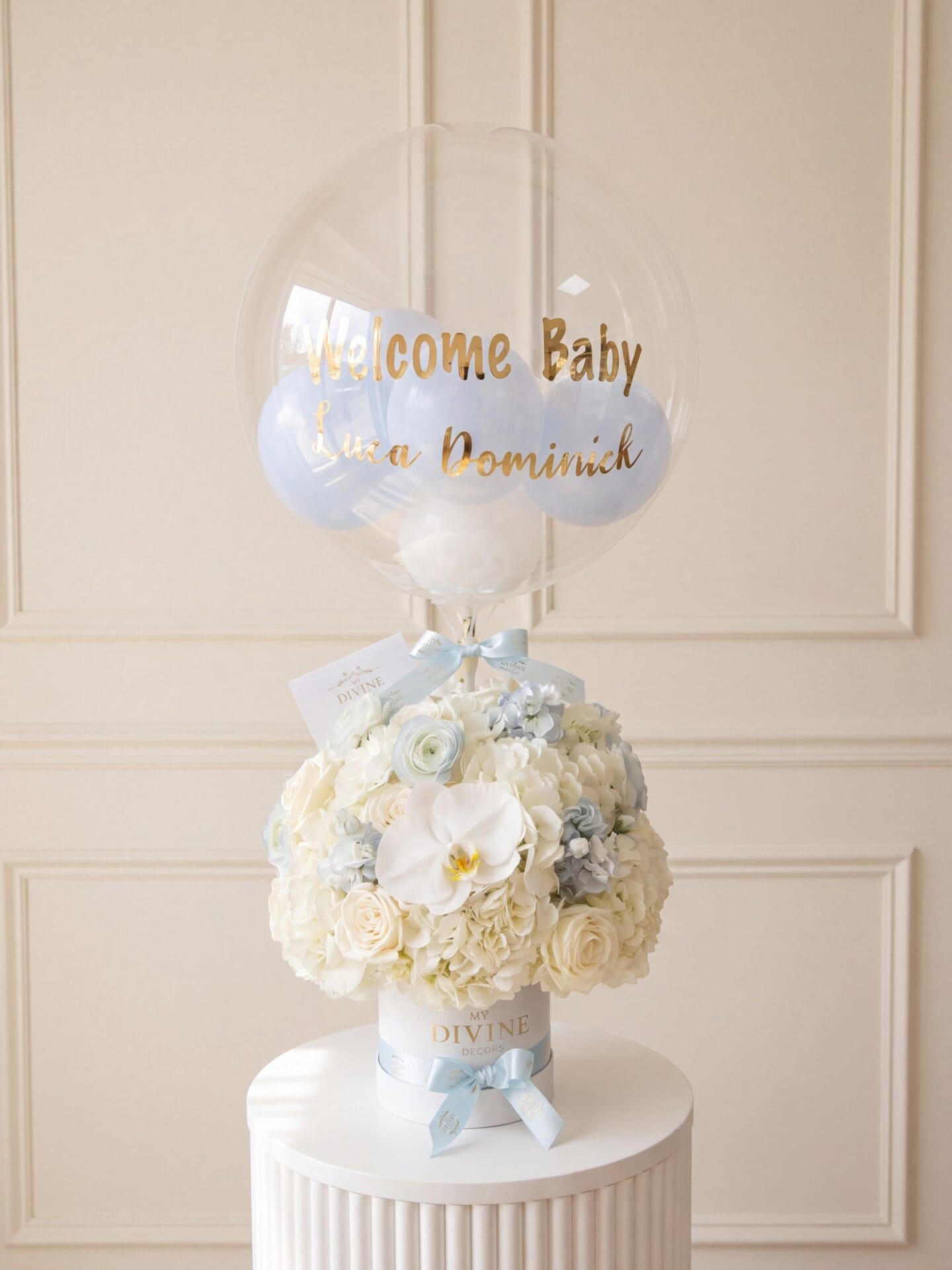 Welcome baby arrangement: ivory roses, hydrangea and white orchid in a white box with blue ribbon and bubble balloon Arreglo de bienvenida al bebé: rosas marfil, hortensias y orquídea blanca en caja blanca con cinta celeste y globo burbuja