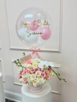 Caja rosada con perlas, rosas, hortensias, rama de orquídea y globo burbuja de cumpleaños