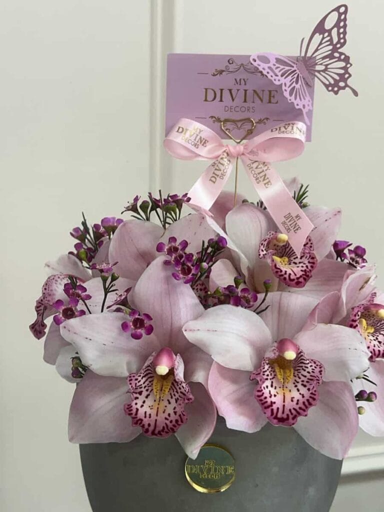 Pink cymbidium orchids in a stone pot with a My Divine Decors card
