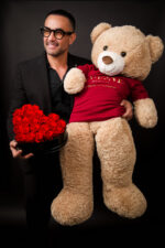 Nelson Ramirez holding a custom teddy bear dressed in a My Divine Decors branded shirt with a heart of red roses