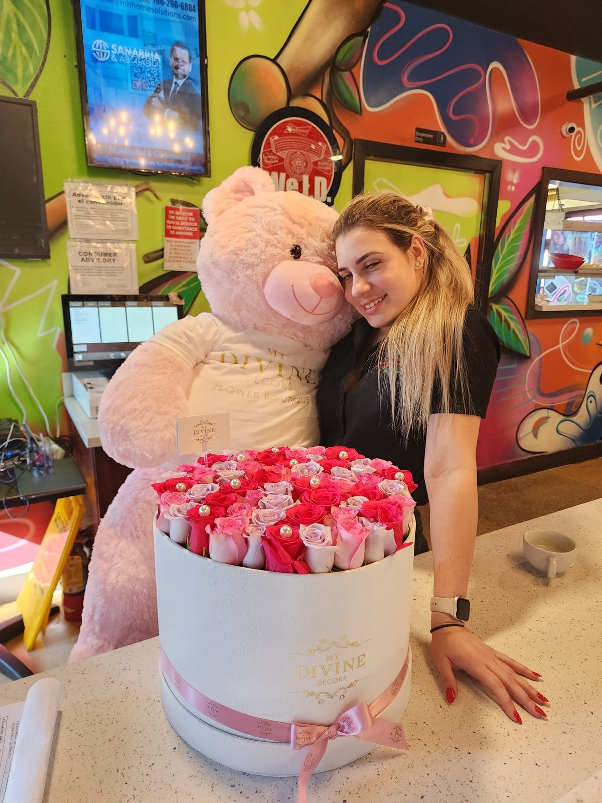 Woman hugging a giant pink teddy bear behind a large box of roses, showing its real size