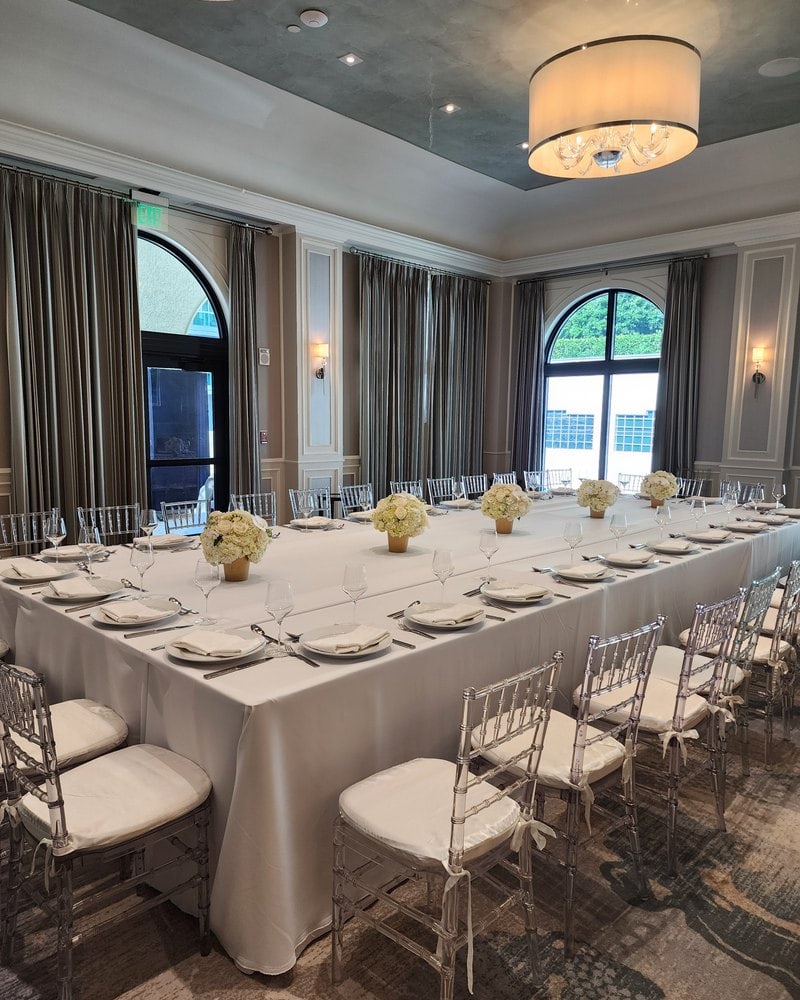 White rose centerpieces on a long banquet table in a Miami ballroom