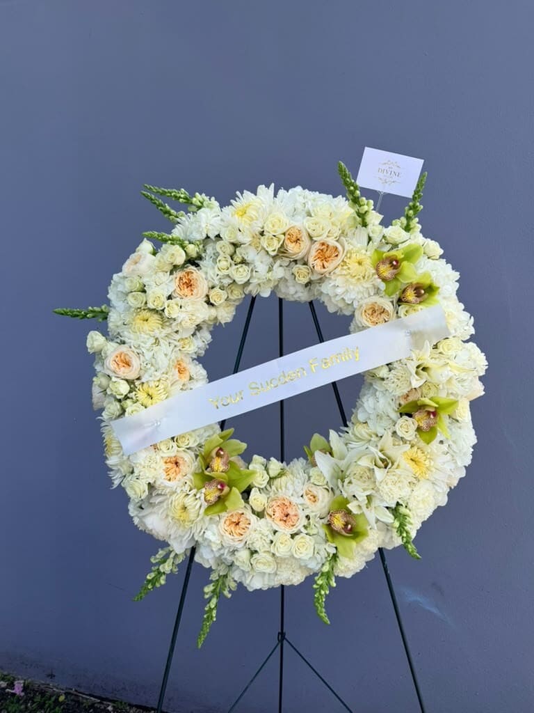 Corona funeraria marfil con rosas durazno, orquídeas cymbidium verdes y cinta personalizada en su caballete