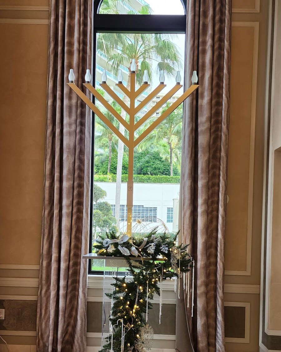 Gold menorah dressed with a garland of greenery and white flowers in a Miami lobby