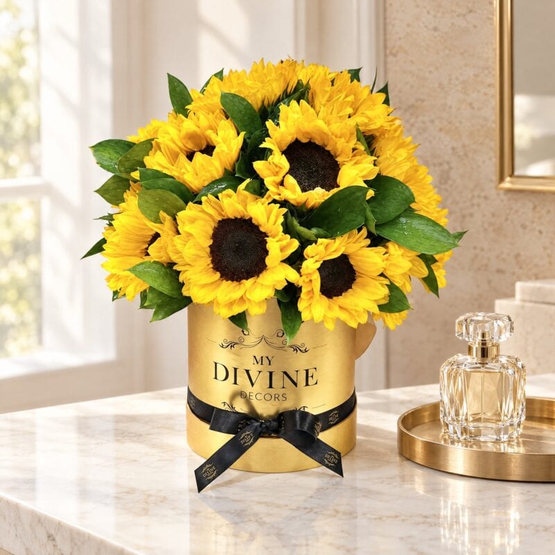 Medium Sunflower Round in a gold box with black ribbon on a marble vanity