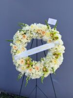 Corona funeraria marfil con rosas durazno, orquídeas cymbidium verdes y cinta personalizada en su caballete