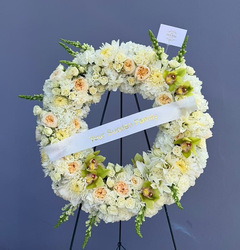 Royal Ivory funeral wreath with ivory and peach roses, green cymbidium orchids and a personalized ribbon on its easel