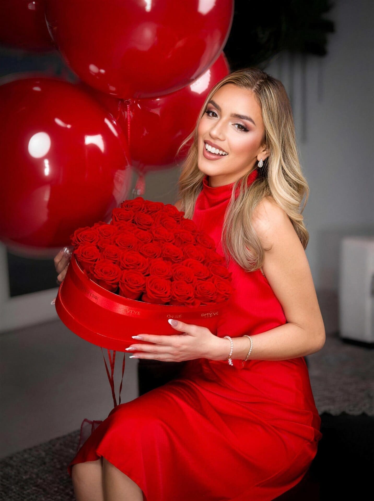Woman in a red dress holding a red rose box from My Divine Decors with red heart balloons behind her