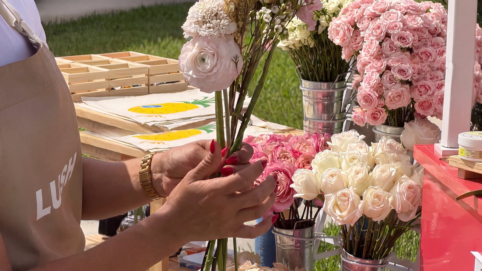 Florista armando un ramo de ranúnculos, rosas y astilbe junto a un carrito de flores con la marca del cliente, en una activación de marca en Miami de My Divine Decors
