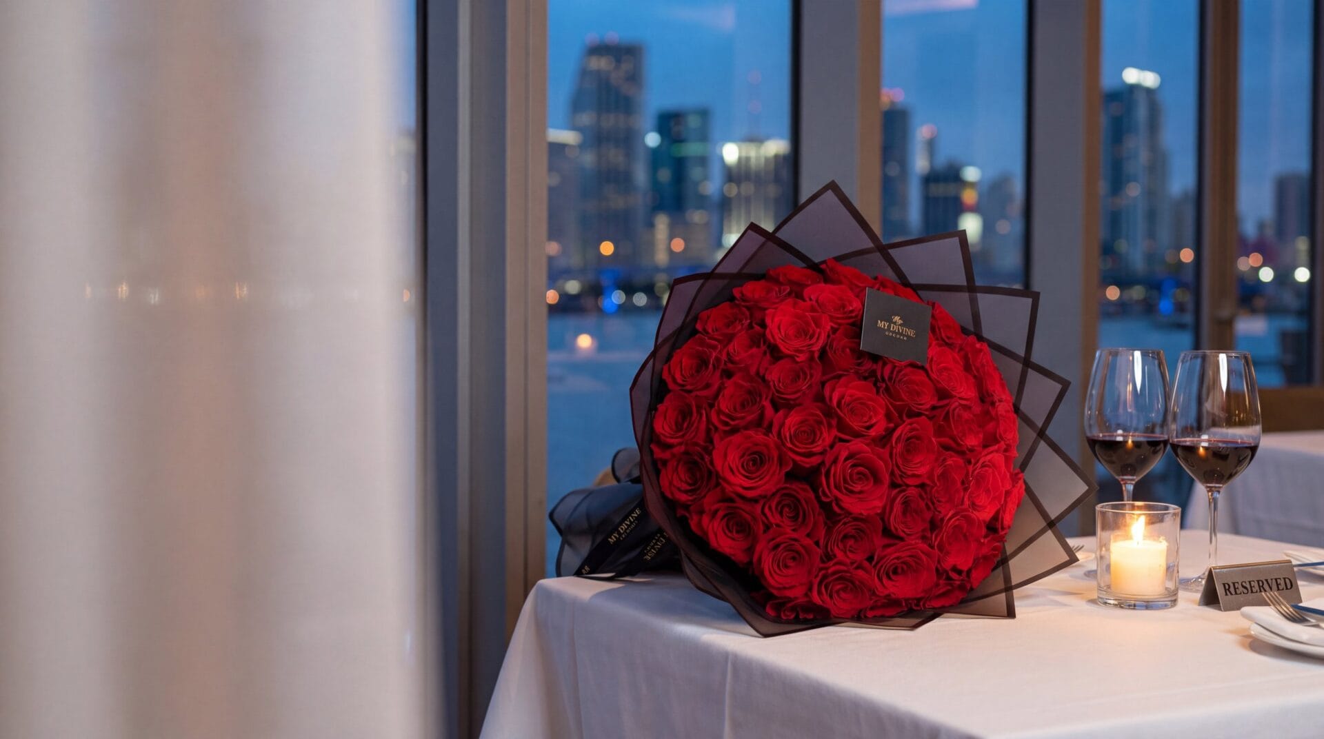Ramo buchon of deep red roses in black wrap by My Divine Decors on a restaurant table set for an anniversary dinner, with the Miami skyline at night
