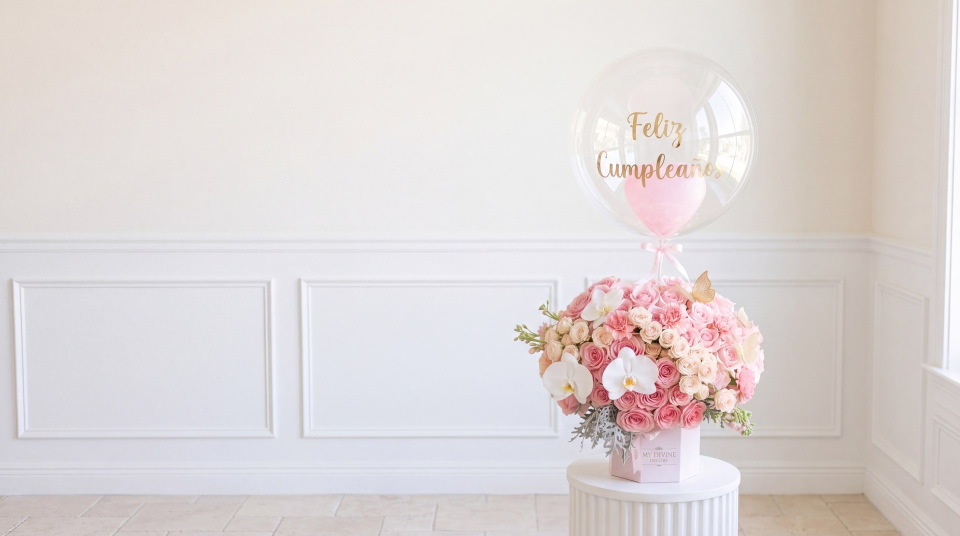 Arreglo de rosas rosadas y orquídeas blancas en caja MY DIVINE DECORS con globo burbuja de Feliz Cumpleaños, sobre un pedestal blanco en la floristería My Divine Decors en Doral