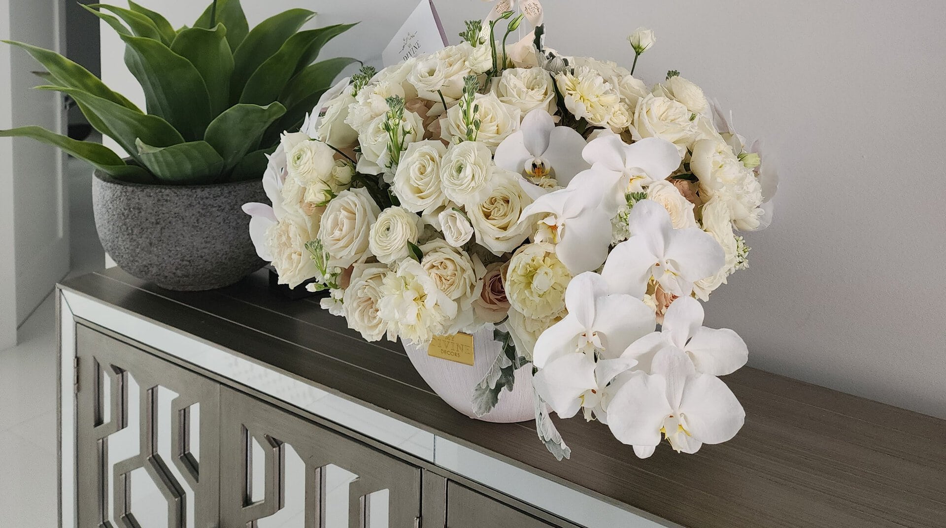 A My Divine Decors birthday arrangement of white roses, garden roses and white orchids on a mirrored console in a Miami home
