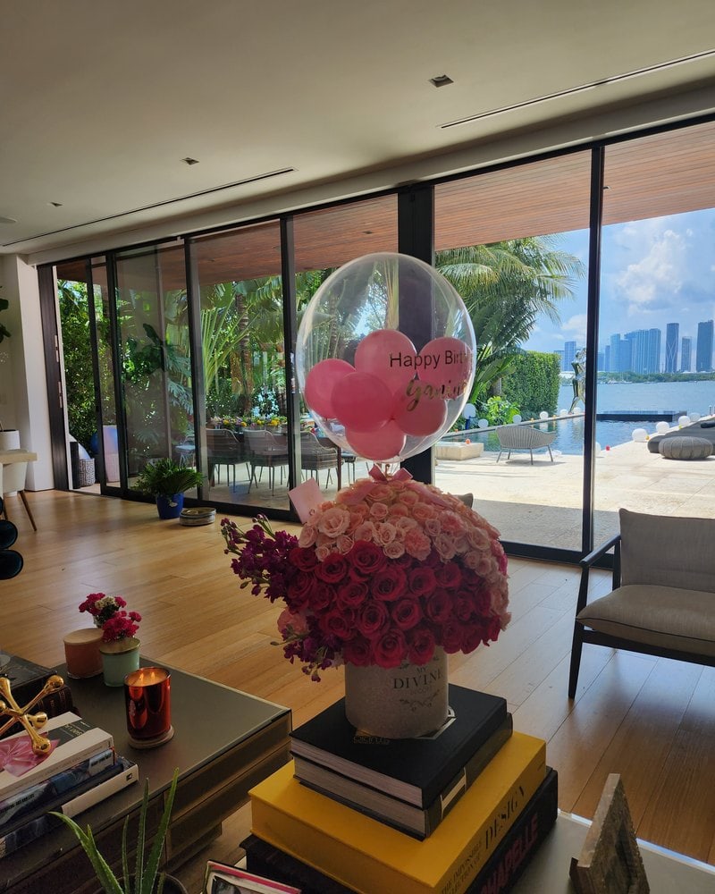 Globo burbuja de cumpleaños con globitos rosados sobre una cúpula grande de rosas rojas en una sala de Miami