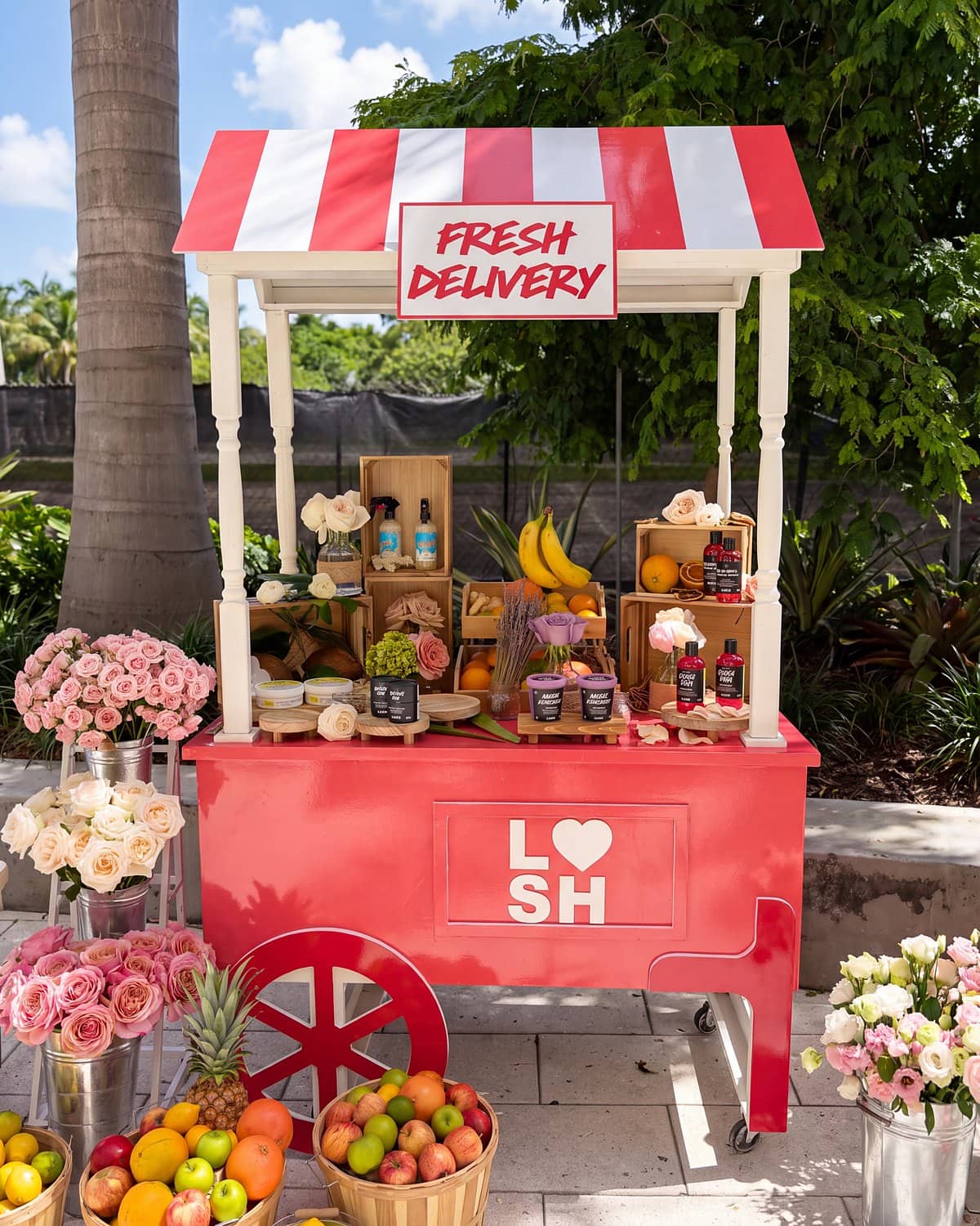 Red branded flower cart with a striped awning, wooden crates of product and fresh flowers at a Miami brand activation