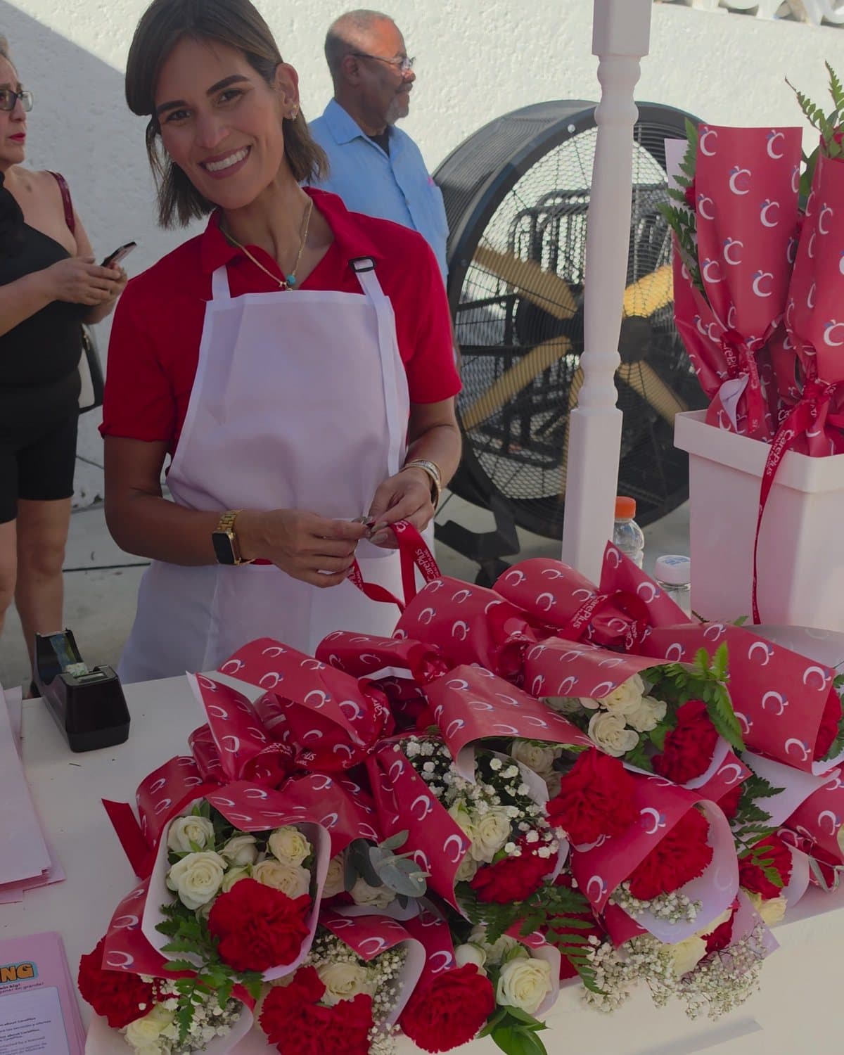 Florist in a red polo and white apron smiling behind petite bouquets wrapped in CarePlus paper at the Miami Beach Bandshell flower bar