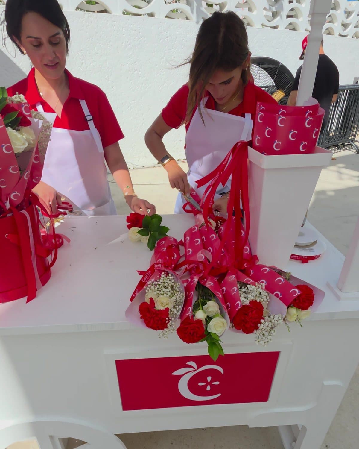Carrito blanco del flower bar con el logo de CarePlus y dos floristas armando ramitos en el Miami Beach Bandshell
