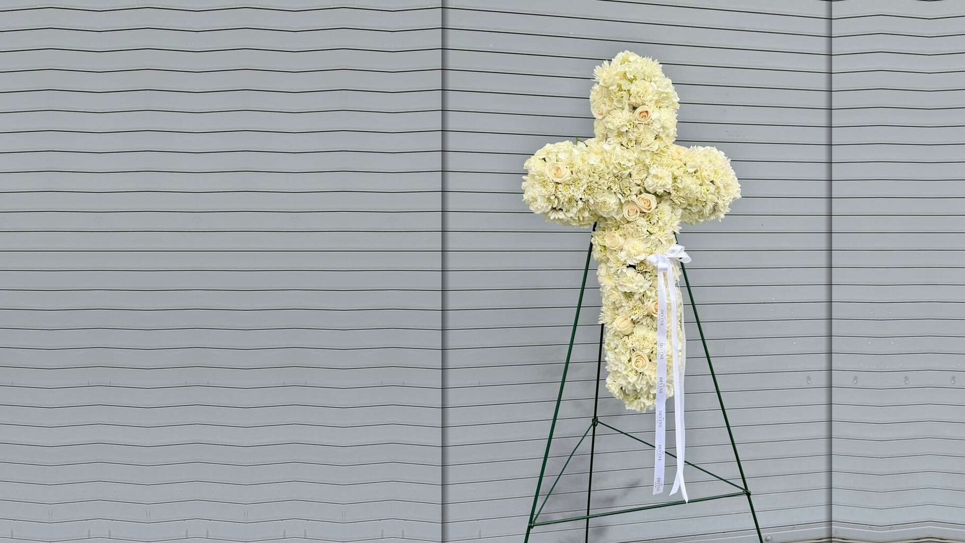 Cruz de flores Heavenly de My Divine Decors: claveles y rosas marfil en su caballete con cinta blanca