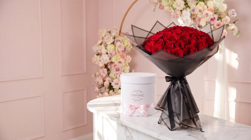 Ramo buchón de rosas rojas junto a una caja sombrero blanca My Divine Decors en el mostrador de la floristería
