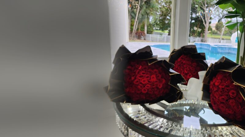 Tres ramos buchón de rosas rojas con papel negro y borde dorado de My Divine Decors sobre una mesa de cristal junto a una piscina en Miami