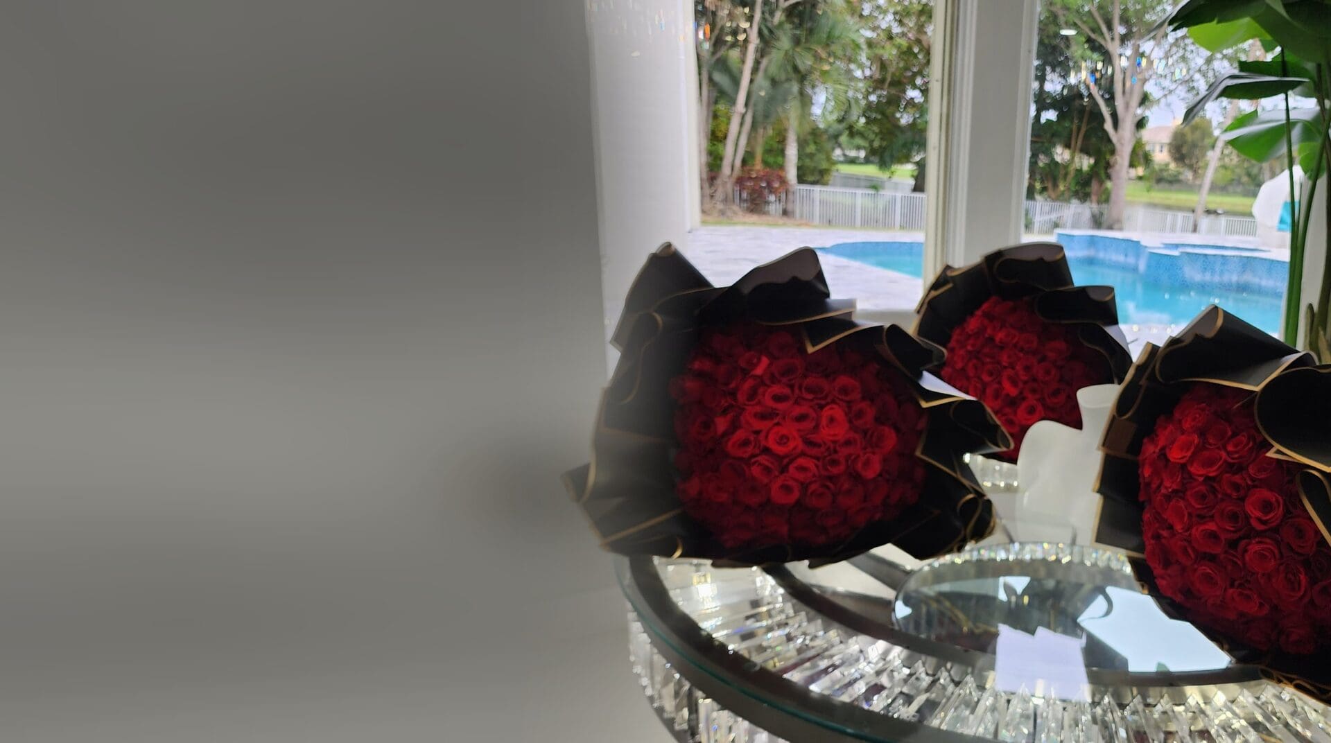 Tres ramos buchón de rosas rojas con papel negro y borde dorado de My Divine Decors sobre una mesa de cristal junto a una piscina en Miami