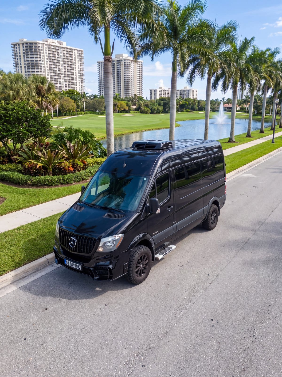Camioneta Mercedes negra de My Divine Decors con placa MY DIVINE en un bulevar con palmas junto al campo de golf y las torres de Aventura