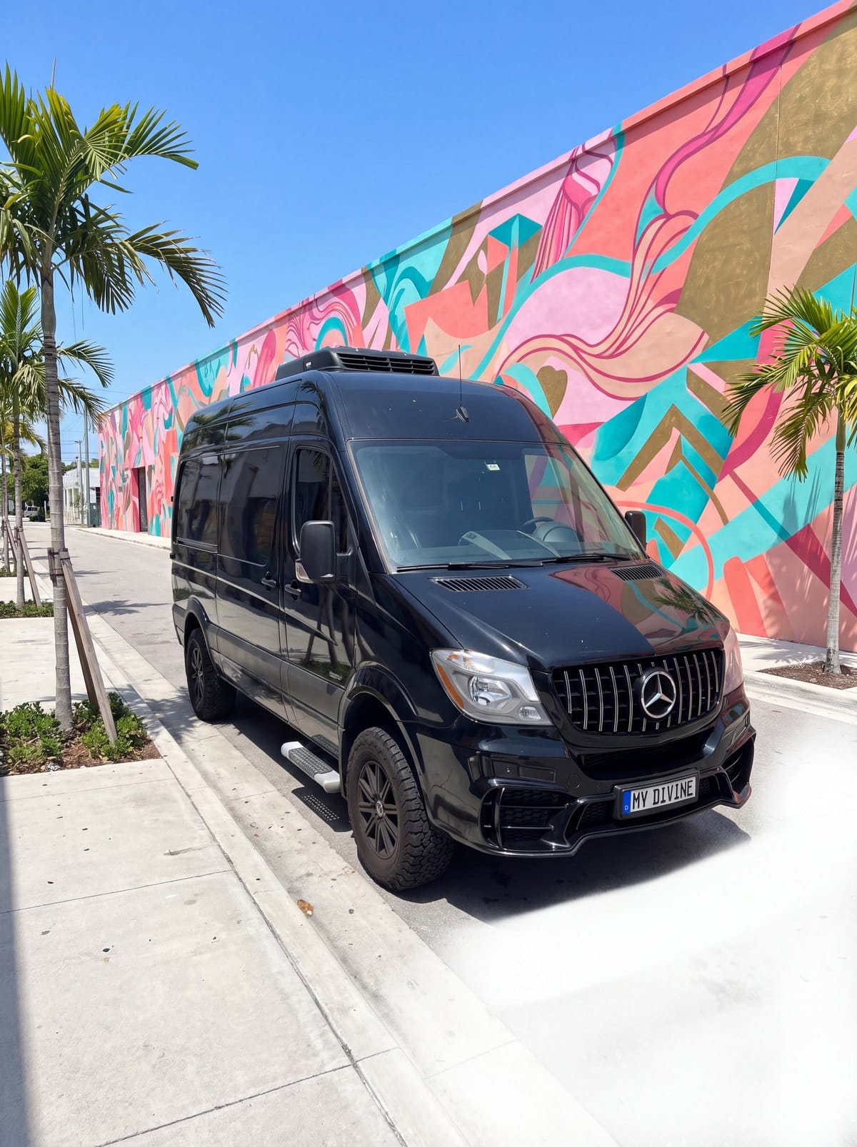 Camioneta Mercedes negra de My Divine Decors con placa MY DIVINE frente a un mural de colores en una calle de Wynwood