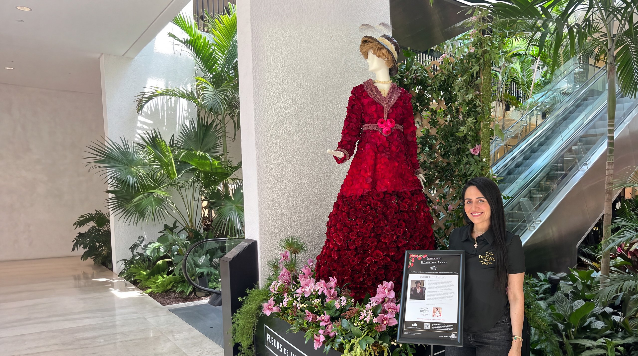 Maniquí de Isobel Crawley vestido de rosas rojas frescas sobre una jardinera de orquídeas rosadas, hecho por My Divine Decors para Fleurs de Villes Downton Abbey en Bal Harbour Shops, con nuestra diseñadora al lado