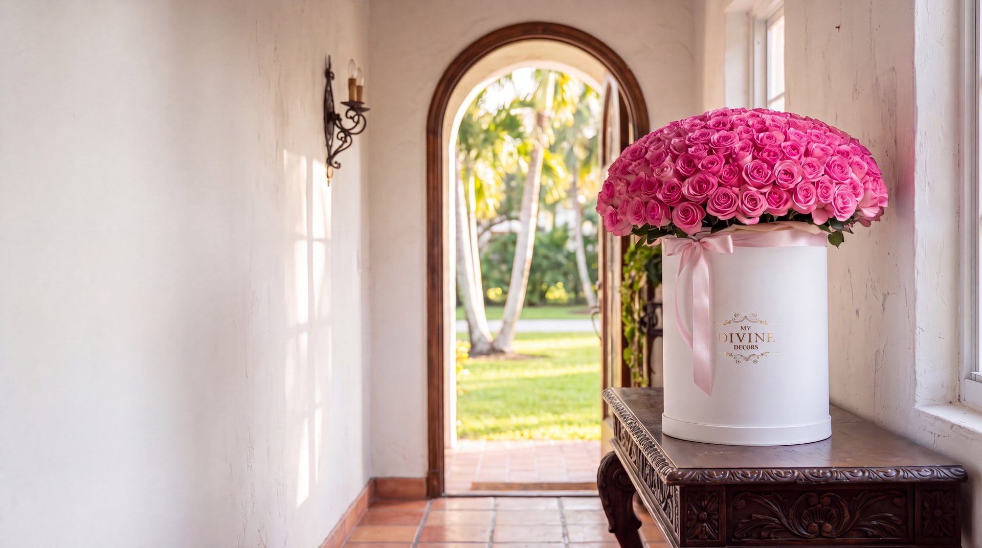Caja redonda alta blanca de My Divine Decors con 200 rosas rosadas sobre una consola de madera tallada en el recibidor de una casa mediterránea en Miami Springs