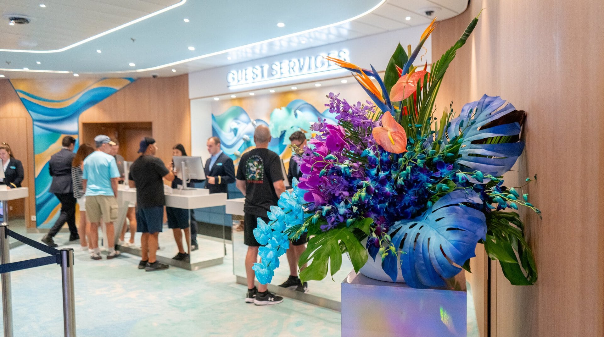 Arreglo de orquídeas moradas y azules, anturios y aves del paraíso de My Divine Decors junto a Guest Services del Star of the Seas de Royal Caribbean