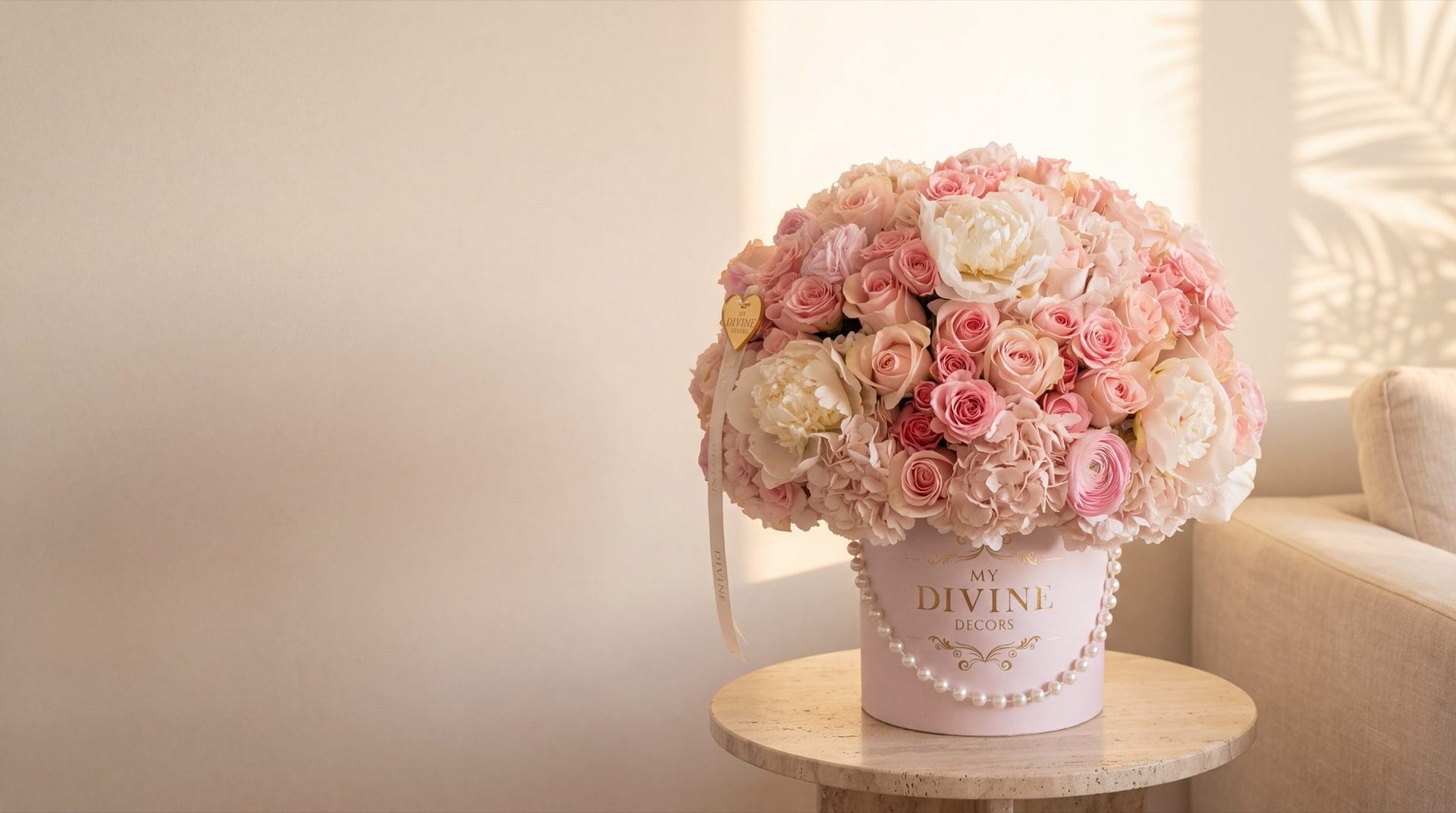 Arreglo Deluxe Pink Bloom de rosas rosadas, peonías blancas, hortensias y ranúnculos en caja sombrero rosada de My Divine Decors con perlas, sobre mesa de travertino