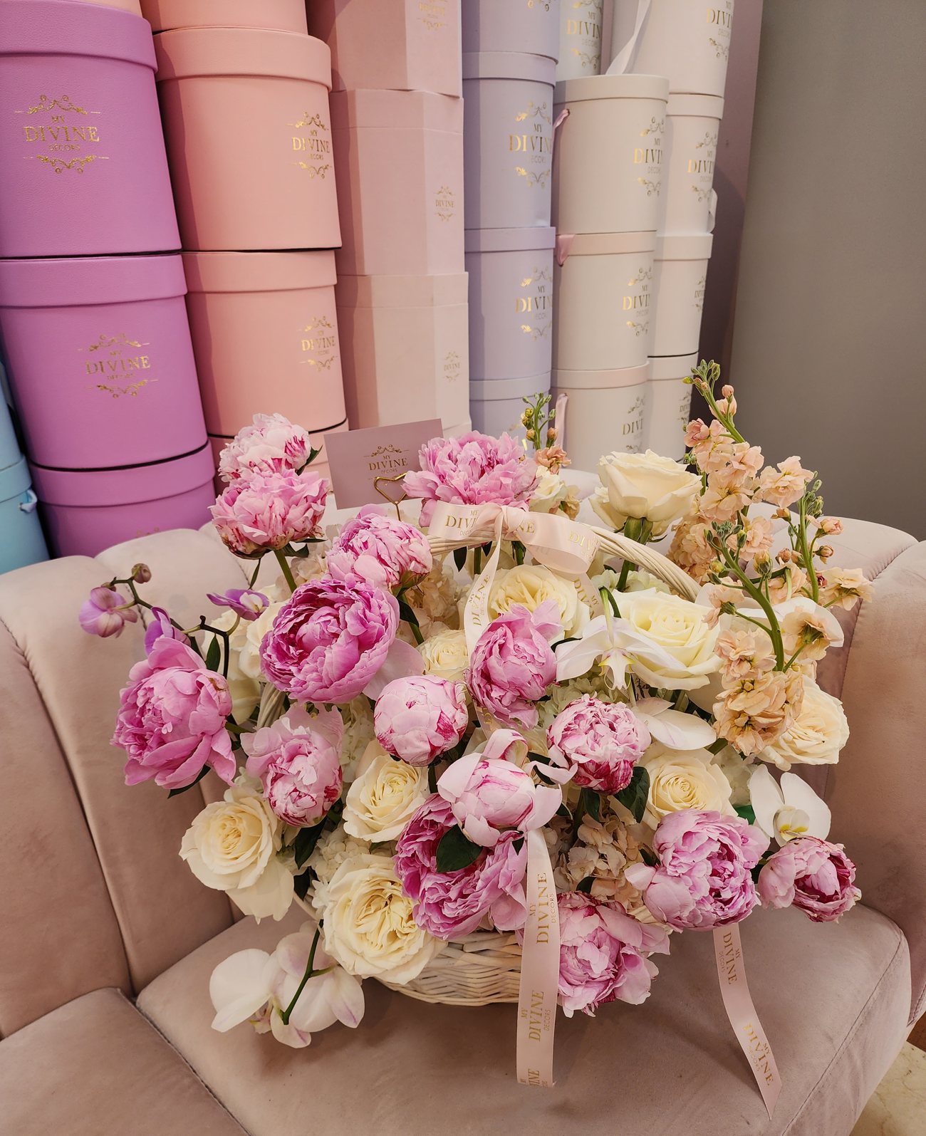 Canasta de peonías rosadas, rosas blancas y orquídeas de My Divine Decors frente a la pared de cajas sombrero del taller