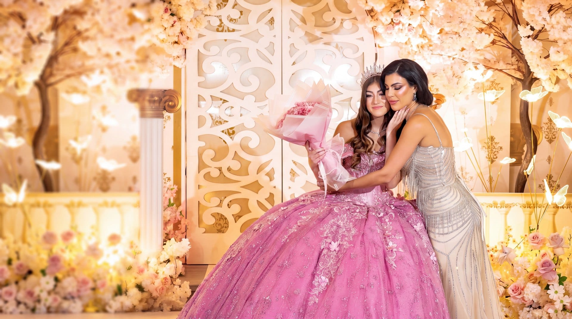 Quinceañera con vestido rosa y su ramo de rosas rosadas abrazada por su mamá en el salón de su fiesta en Miami