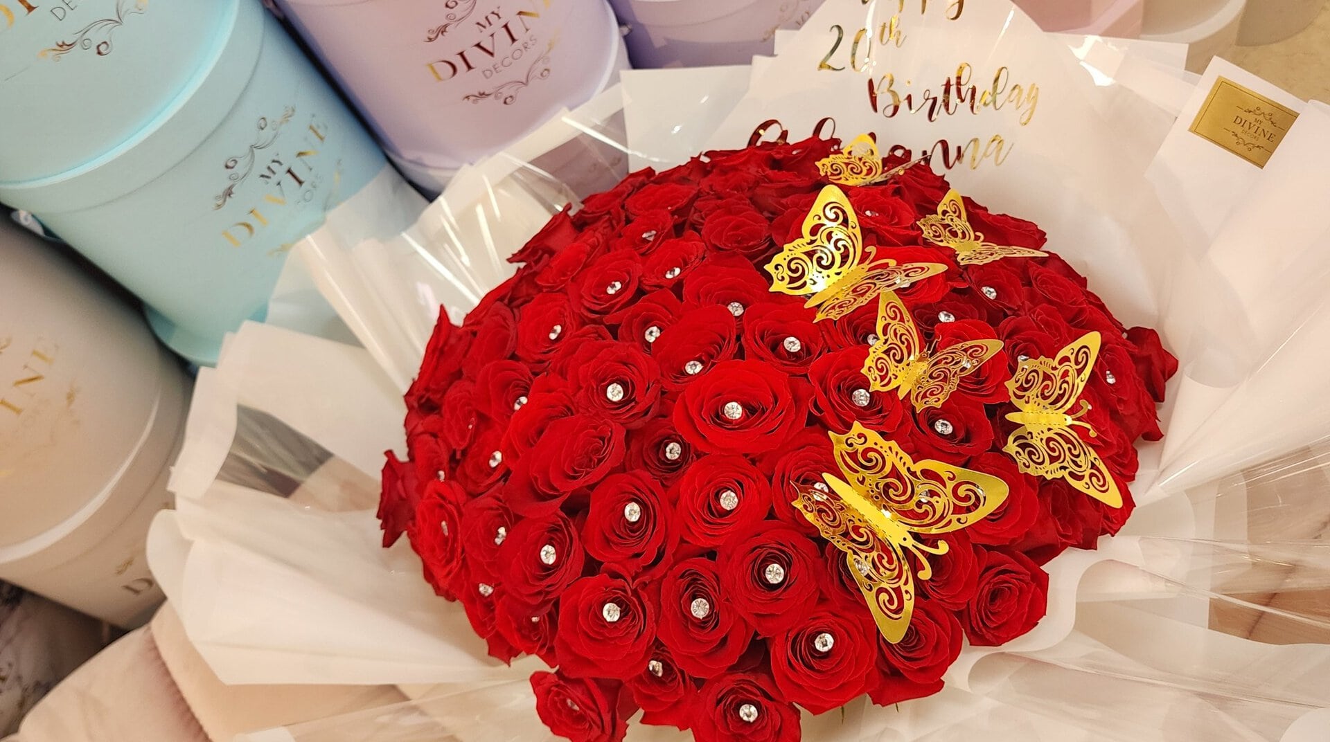 Ramo buchón de rosas rojas con cristales y mariposas doradas frente a las cajas sombrero MY DIVINE de nuestro taller en Doral