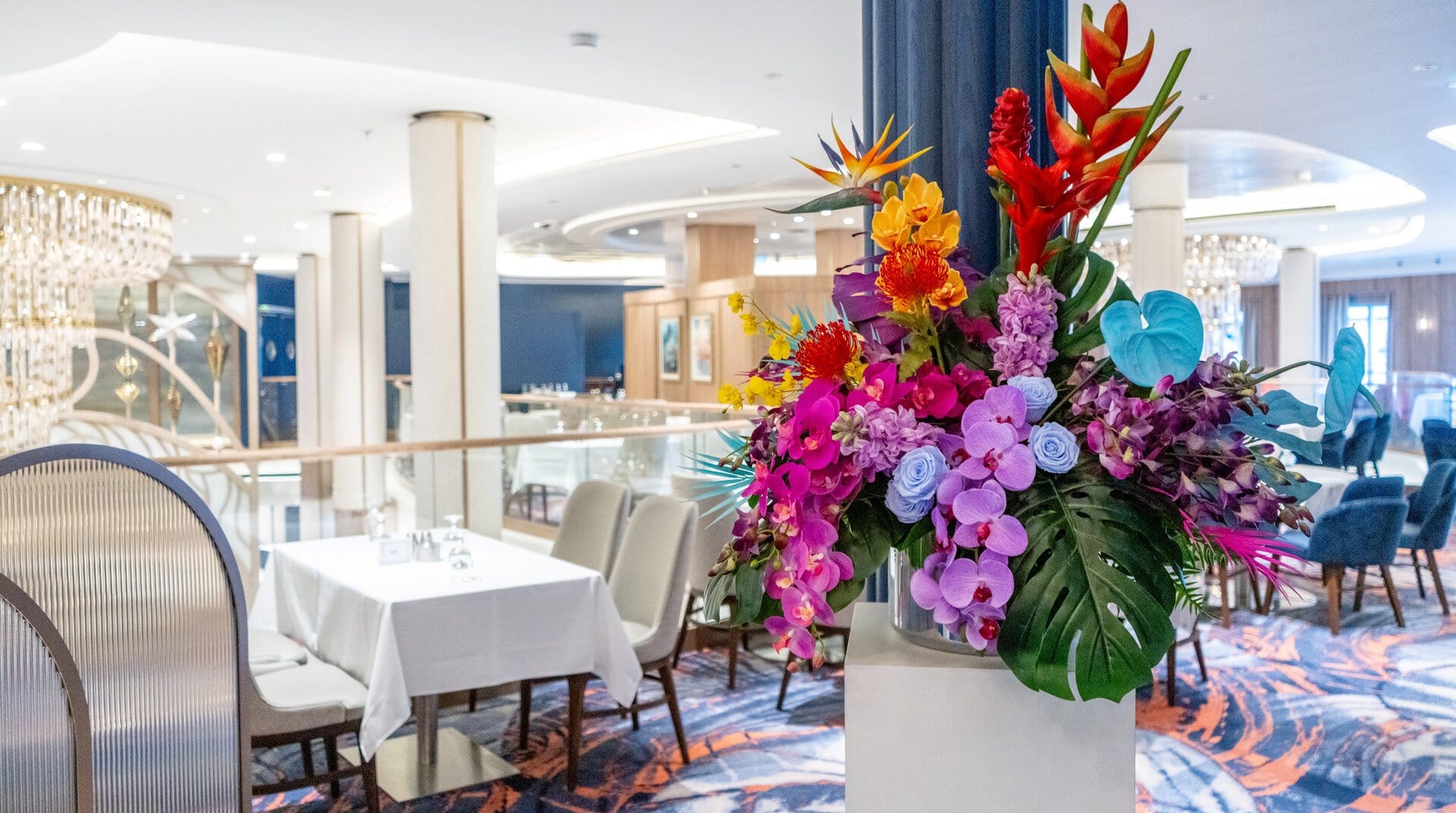 Un arreglo tropical de heliconias, orquídeas y rosas preservadas sobre un pedestal blanco en el comedor principal del Star of the Seas de Royal Caribbean