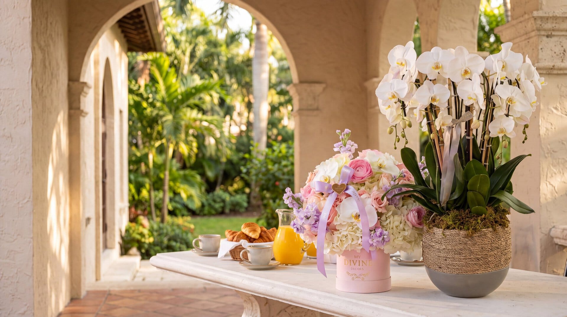 A My Divine Decors Hanna signature box of roses, ranunculus and hydrangeas and a woven planter of white phalaenopsis orchids on a Sunday brunch table on a Coral Gables terrace