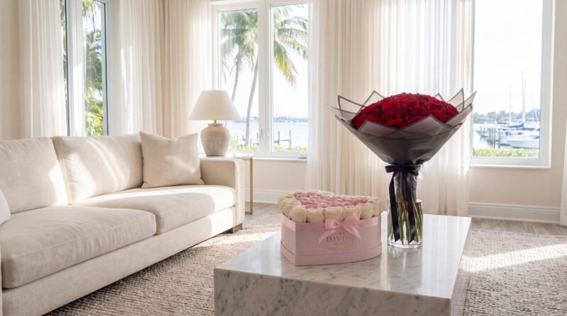 Una caja de corazón rosada de My Divine Decors con rosas blancas y rosadas y un ramo buchón de rosas rojas en un florero de cristal sobre una mesa de mármol en una sala de Coconut Grove un domingo por la mañana