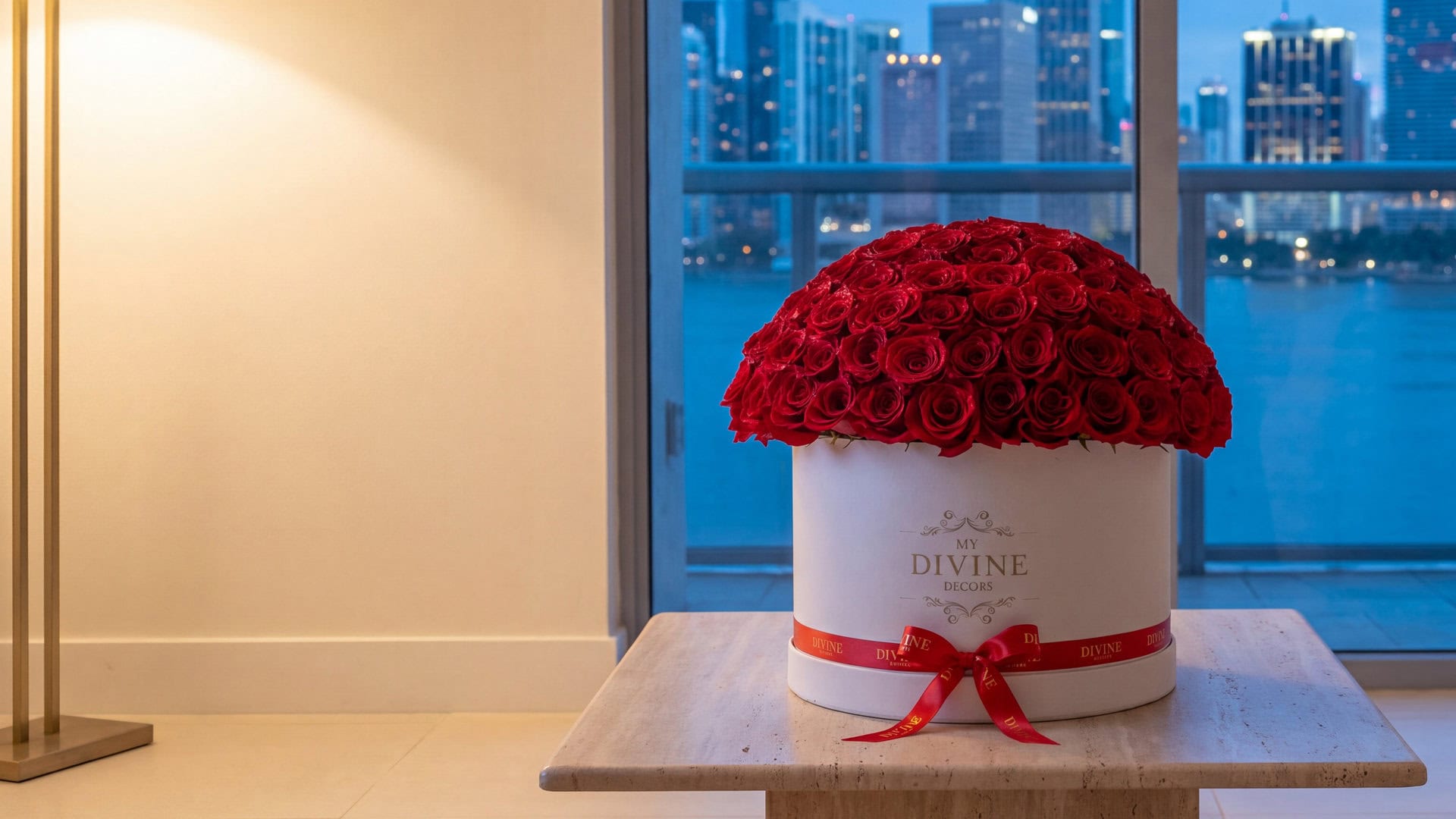 One hundred red roses in a white My Divine Decors Grand Box on a travertine table in a Brickell condo overlooking the bay at dusk