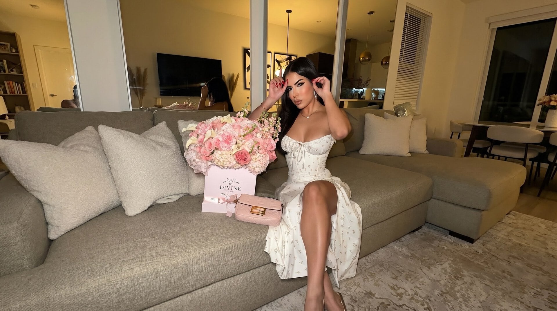 Woman on a sofa in a Miami living room with a pink My Divine Decors box of pink roses, hydrangeas and calla lilies next to her handbag