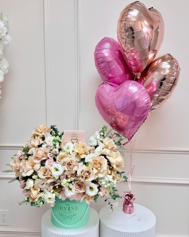 Pink and rose gold foil heart balloons tied to a weight next to peach roses in a hat box