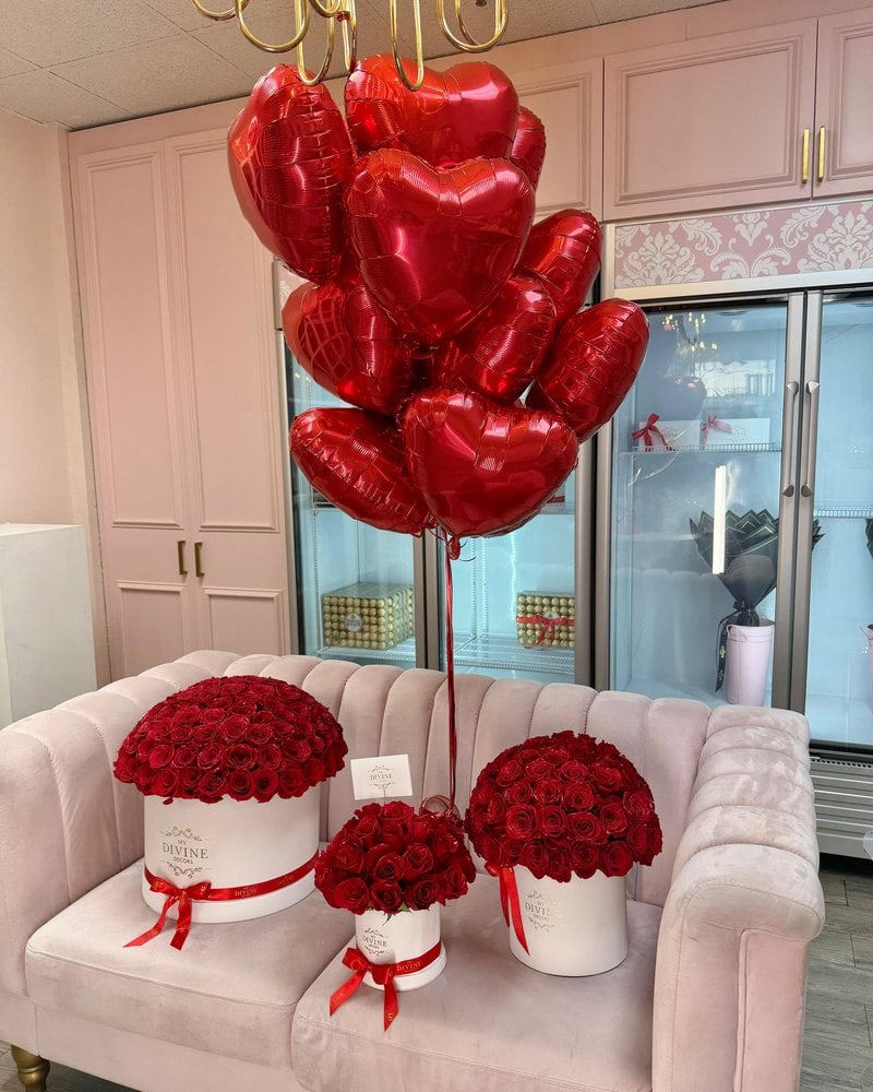 Red heart foil balloon bouquet over a pink velvet sofa with three red rose hat boxes
