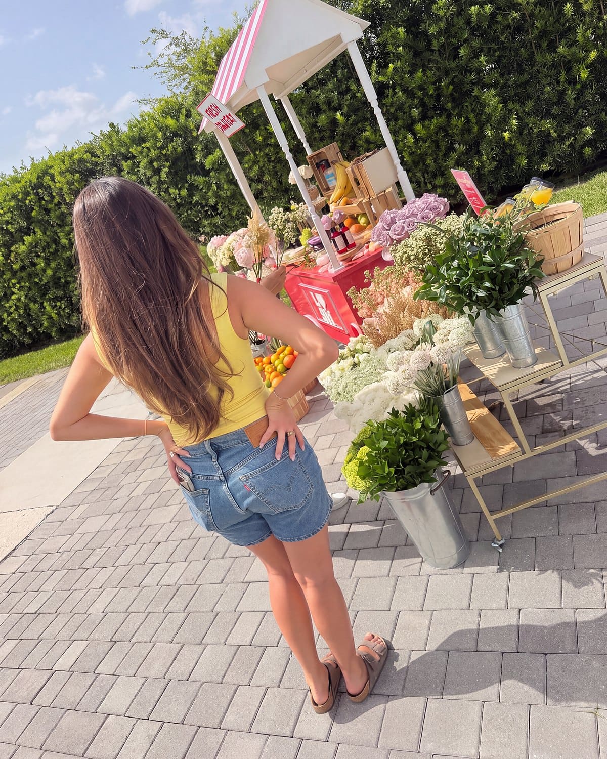 Guest in a yellow top looking at the branded flower cart and its buckets of flowers during an influencer activation in Miami
