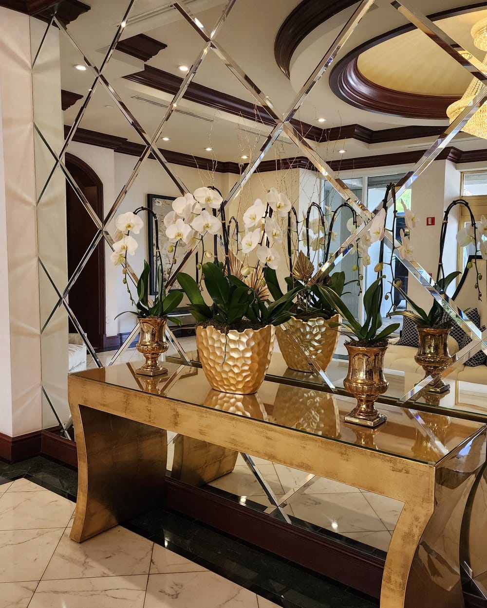 White orchids in gold planters on a gold console in a Miami lobby with mirrored walls