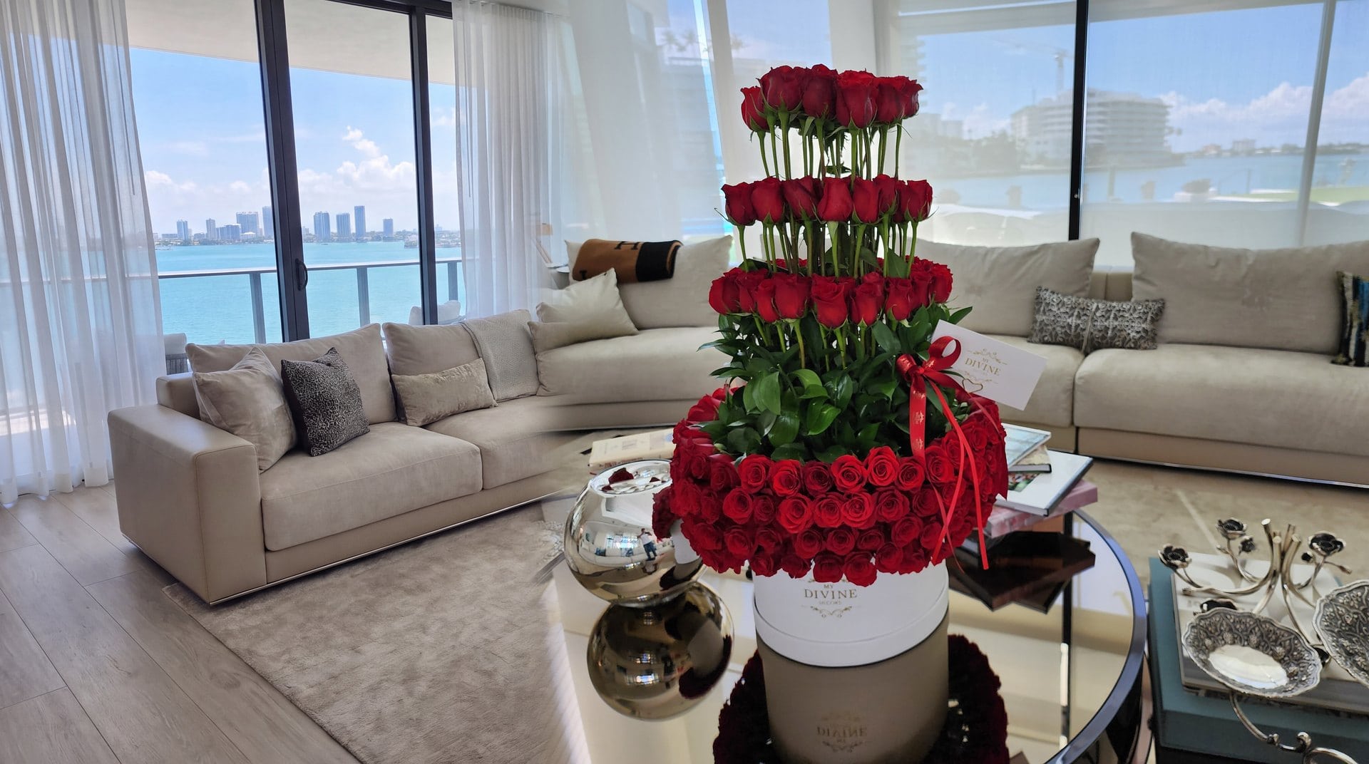 A tower of 200 red roses in a white MY DIVINE DECORS box on a coffee table in a Miami living room overlooking the bay