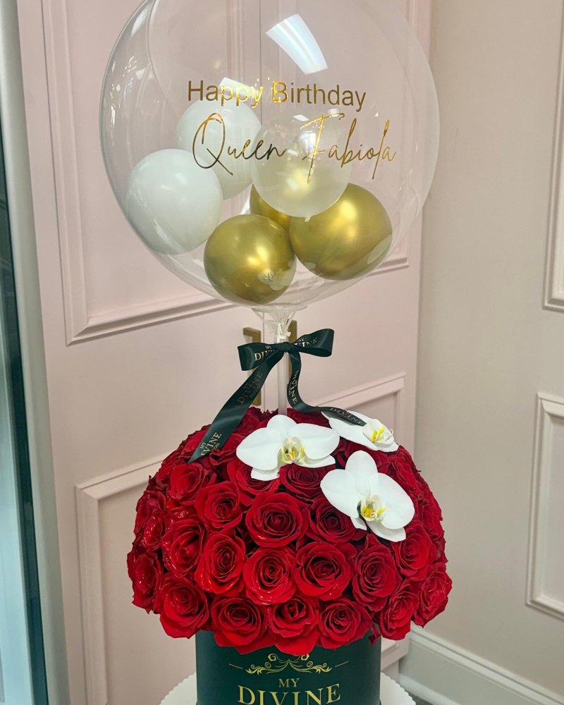 Globo burbuja personalizado con globitos dorados y blancos sobre rosas rojas y orquídeas blancas en caja sombrero verde oscuro