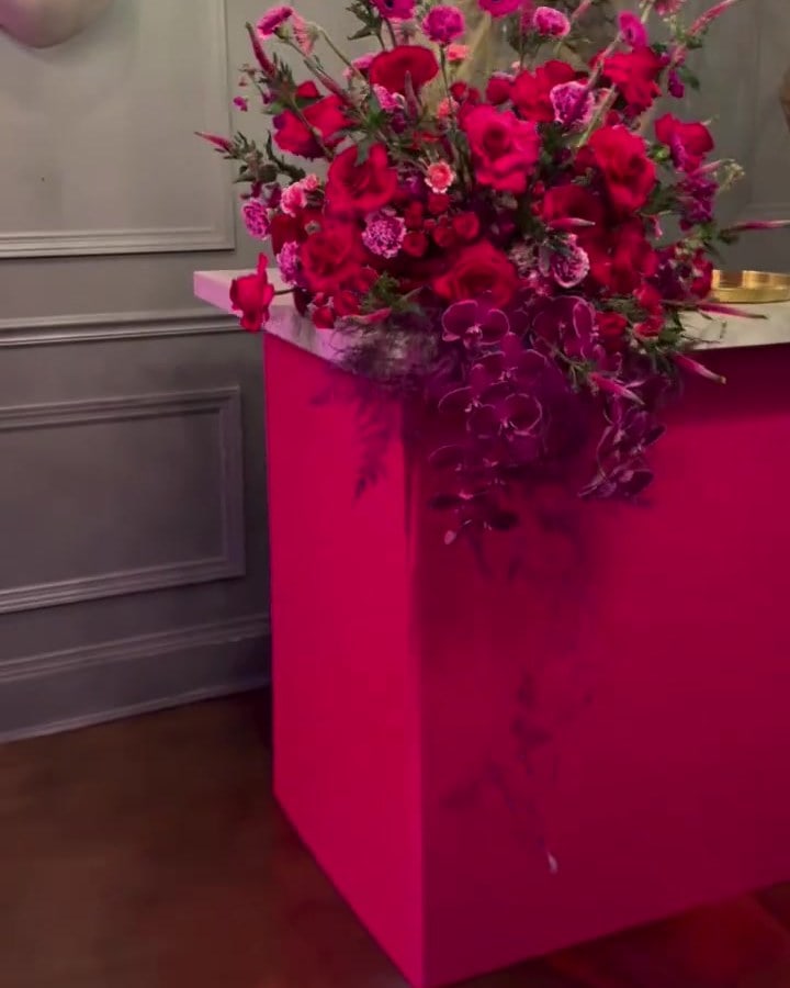 Red rose and orchid arrangement on a magenta pedestal in a grey paneled lounge during Premio Lo Nuestro 2026