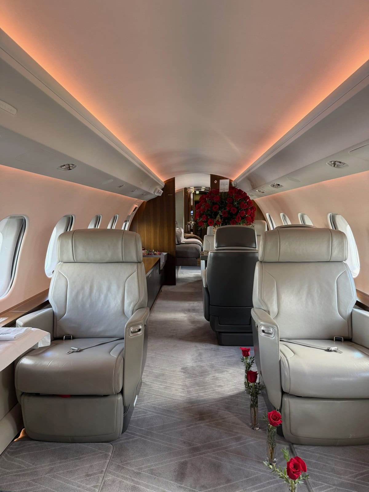 Private jet cabin with cream leather seats, a large arrangement of red roses at the bulkhead and single red roses in clear bud vases along the aisle