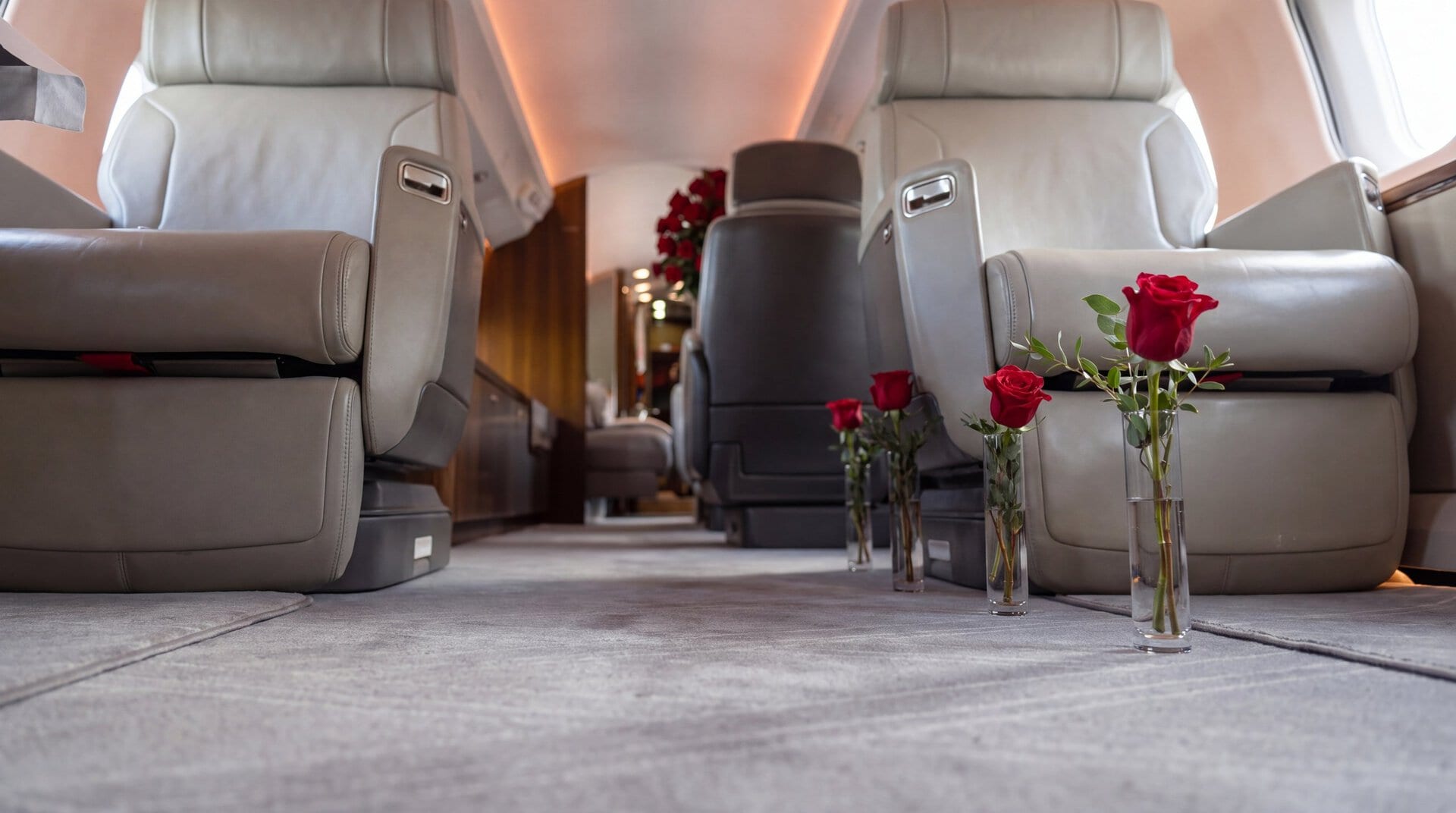 Single red roses in clear bud vases standing on the aisle of a private jet cabin, with a large red rose arrangement at the far end, by My Divine Decors in Miami