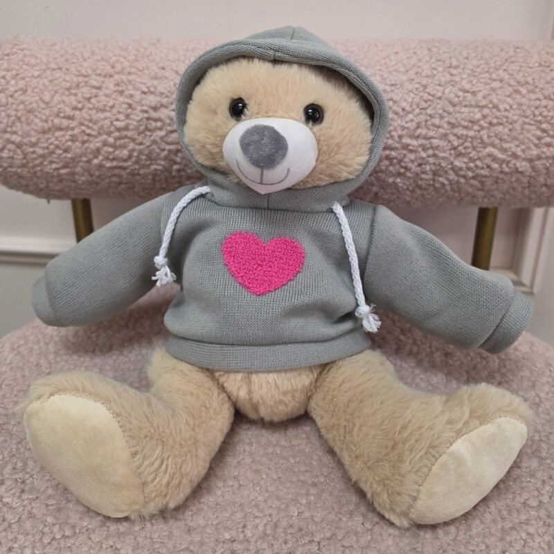 Osito de peluche miel con sudadera gris de cordones blancos y corazón rosado bordado