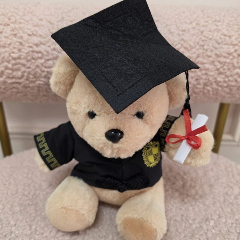 Osito de peluche miel graduado con birrete y toga negra de ribete dorado y diploma